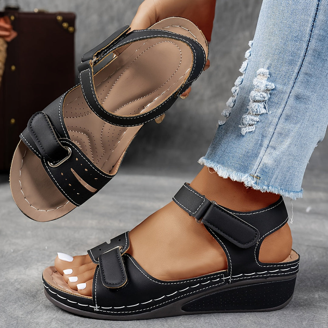 Black wedge sandals worn with light blue jeans on a gray surface