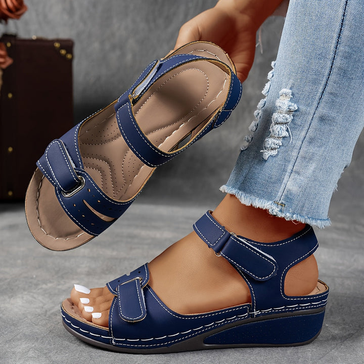 Blue sandals with velcro straps worn by a person on a gray surface.