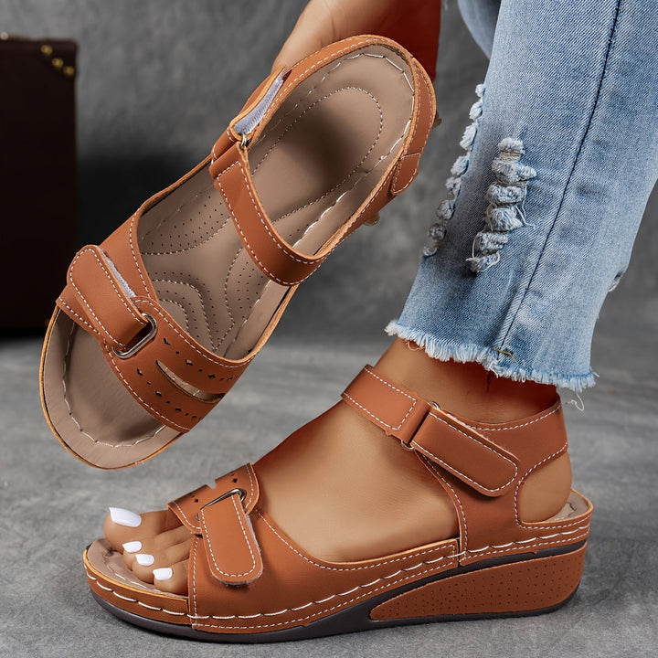 Brown sandals worn with light blue jeans on a gray surface