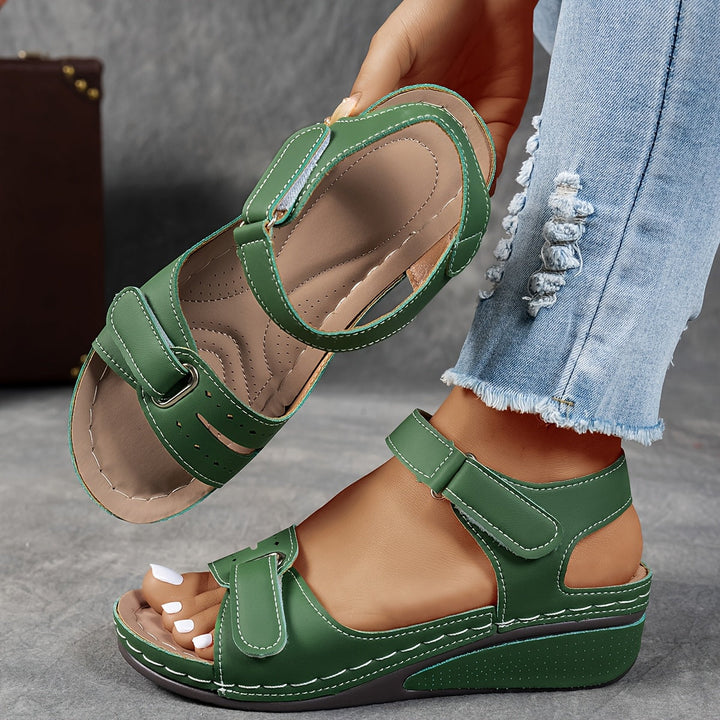 Green sandals worn with light blue jeans on a neutral background