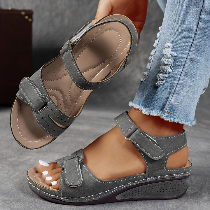 Gray sandals worn with ripped jeans on a neutral background