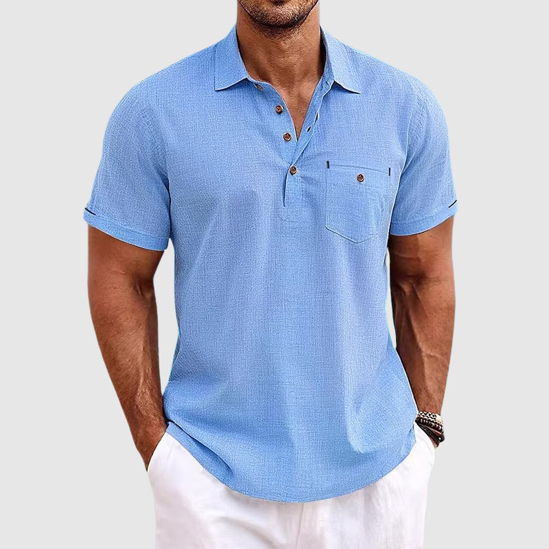 Man wearing a blue patterned polo shirt and white pants on a light gray background