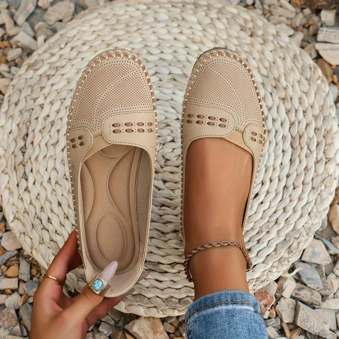 Beige flat shoes being worn on a textured surface with pebbles.