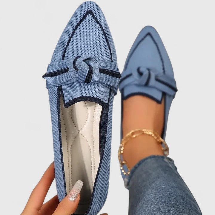 Blue loafers with a knot detail worn by a person on a light gray background