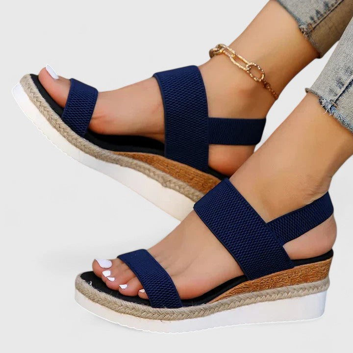 Navy wedge sandals with jute sole worn by a person on a white background