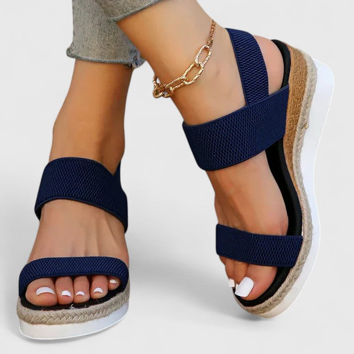 Navy blue sandals with jute sole worn by a person on a light gray background